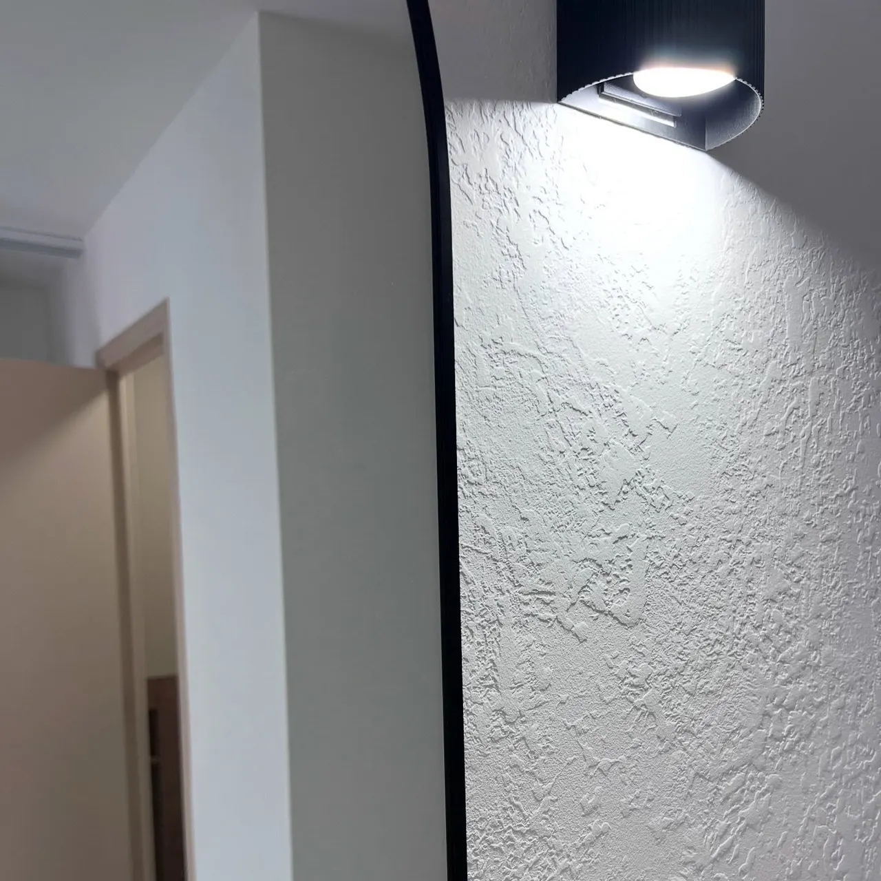 Mit strukturiertem Dekorputz fertiggestellte Wand, von einer Wandleuchte im Streiflicht beleuchtet