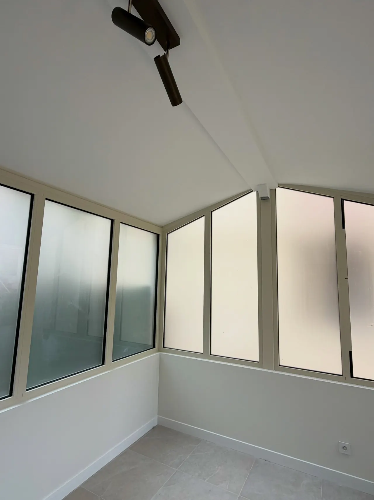 Structure vitrée d'une véranda rénovée, menuiseries et toiture vues de l'intérieur.